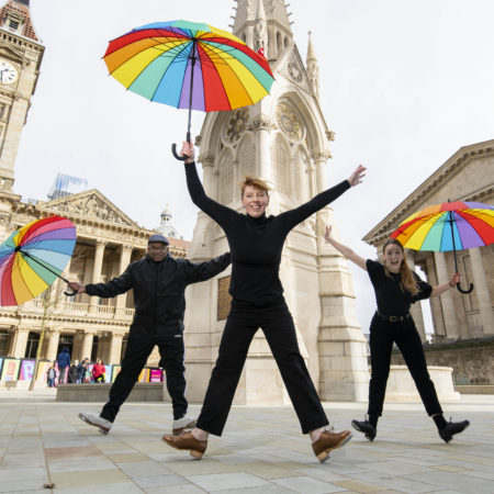 three people holding rainbow umbrellas doing tap dancing